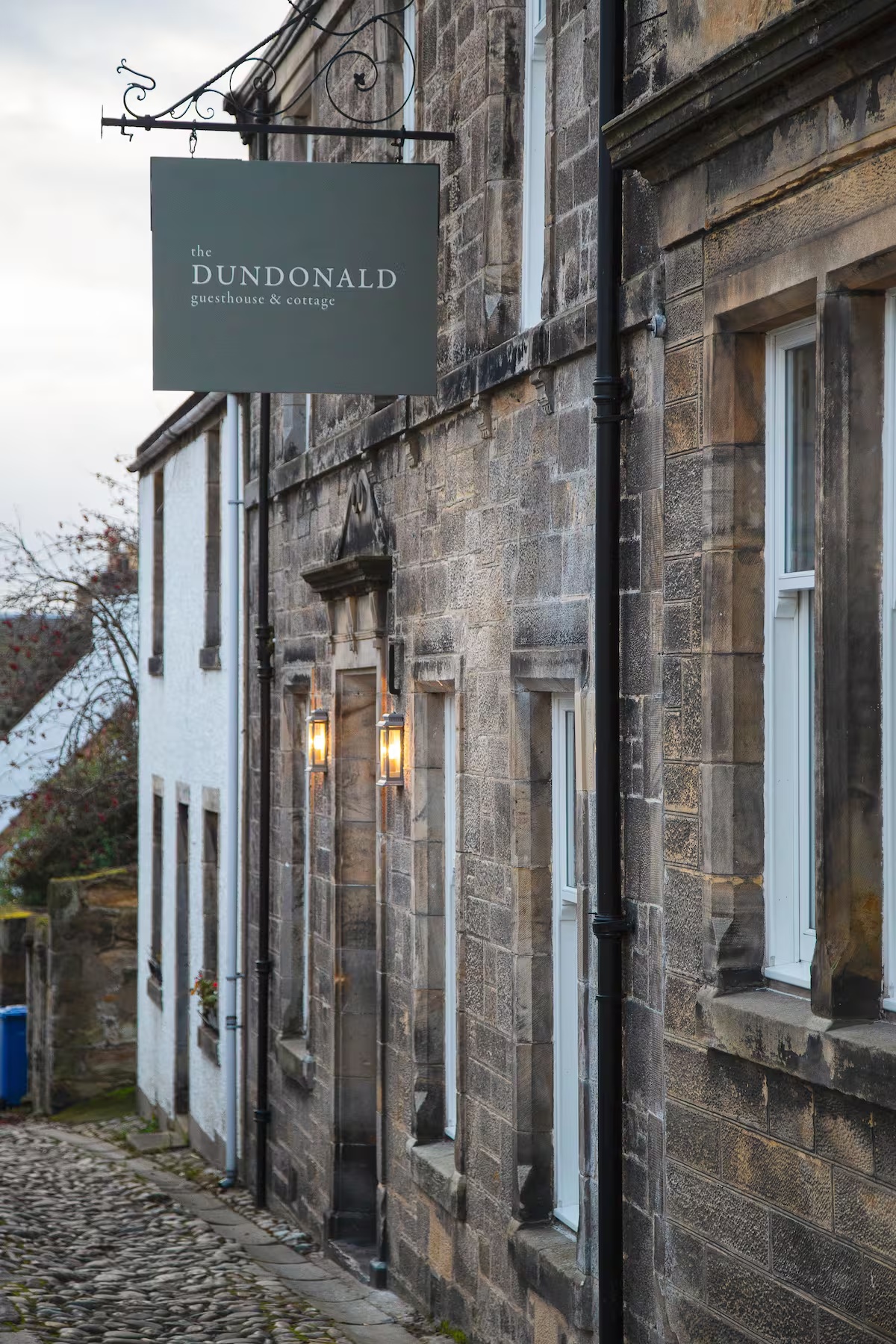 The Dundonald Guesthouse and Cottage sign hanging above a steep cobbled lane in Culross, Kingdom of Fife