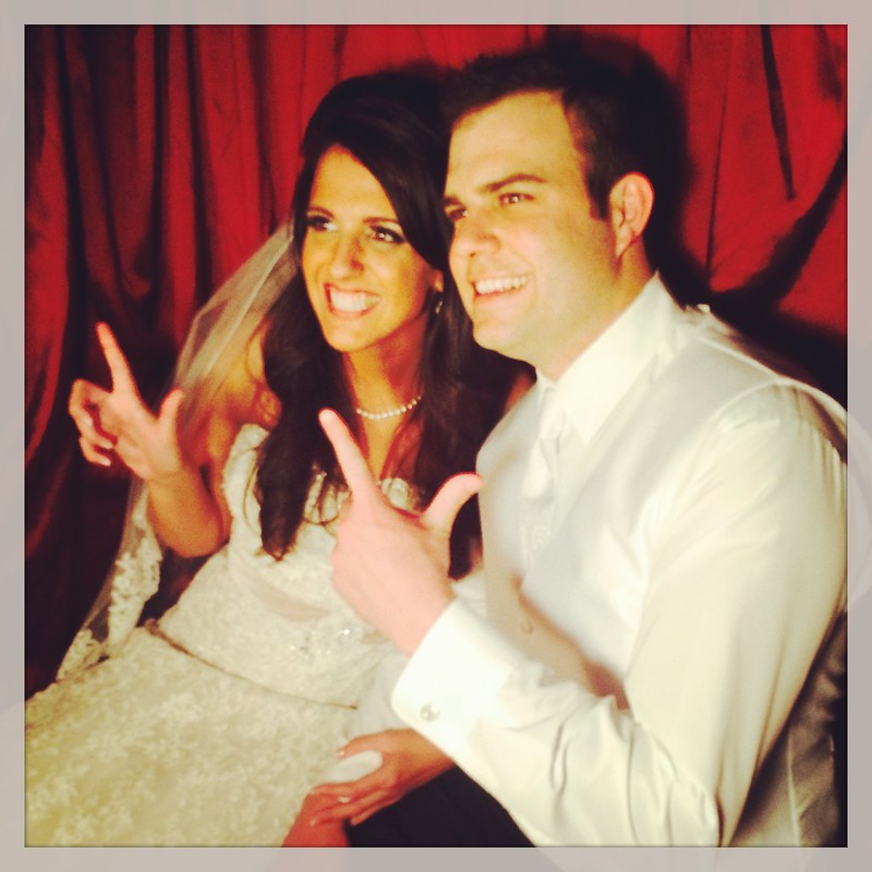 Megan and Jacob smiling in their wedding clothes and making the Guns Up hand sign